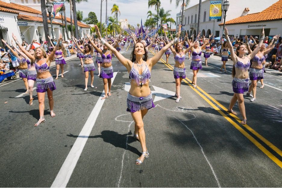 A dance troop in glittery purple costumes walking in the Santa Barbara Summer Solstice parade.