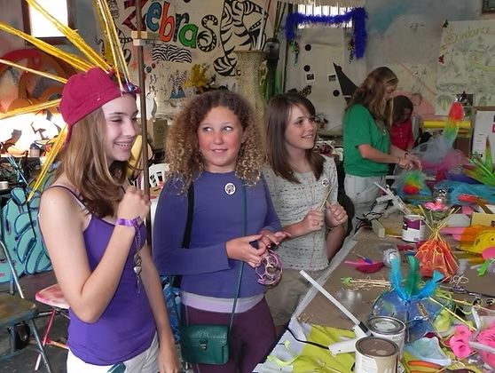 Three young teenage girls in a workshop making colorful costumes.