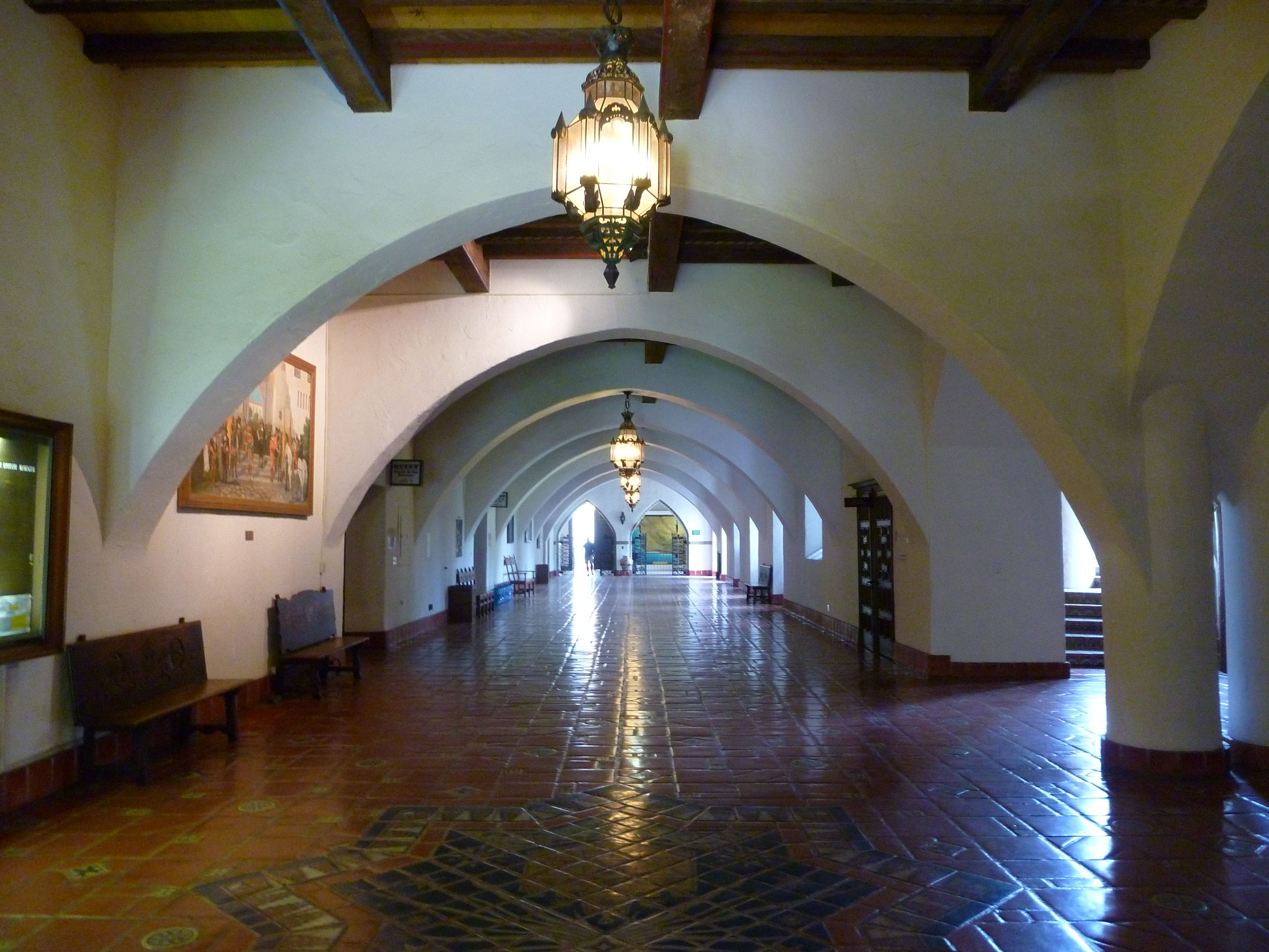 Interior hallway of the Spanish Colonial revival style Santa Barbara County Courthouse, with expansive archways, vintage light fixtures, and polished Saltillo tile floor
