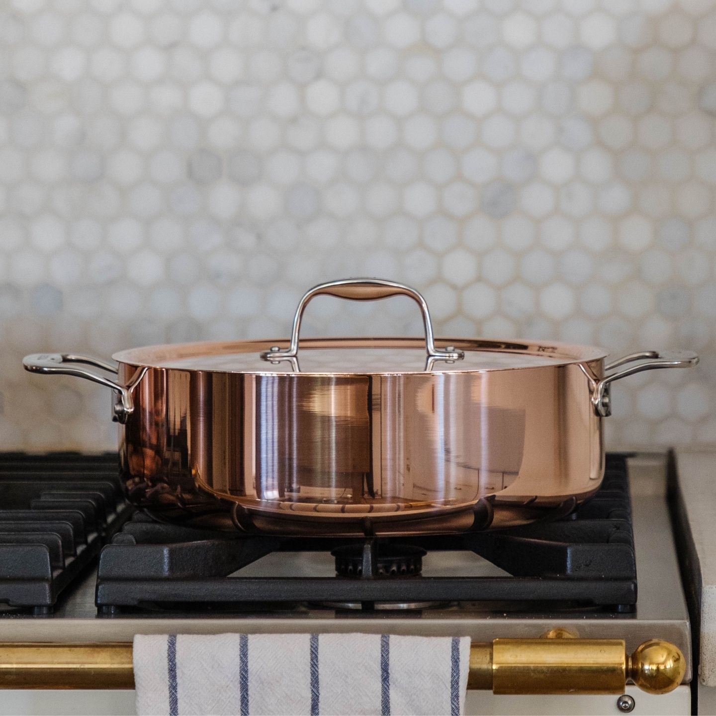 A beautiful, polished, copper-clad roasting pan with lid sitting on a stove burner