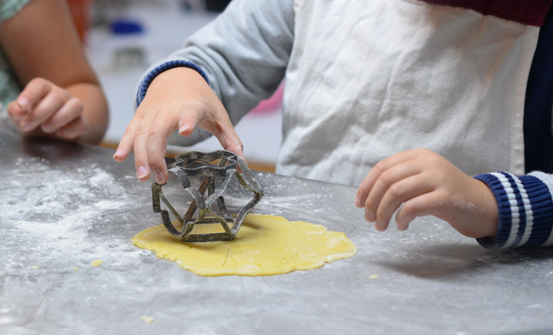 2 kids with a cookie cutter making cookies in a classroom .