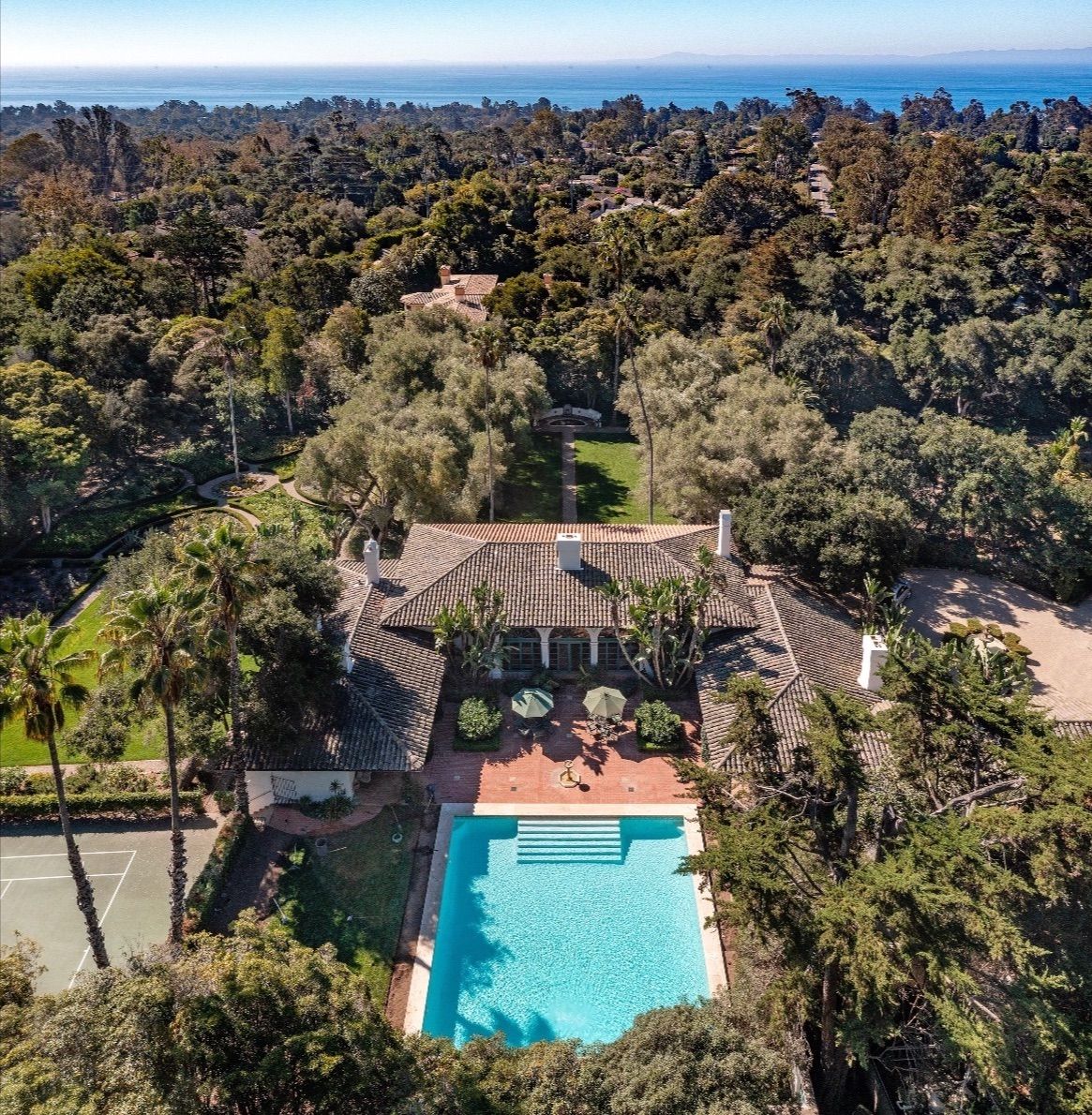 Bird's eye view of a large Montecito estate, with swimming pool, and tennis court surrounded by trees