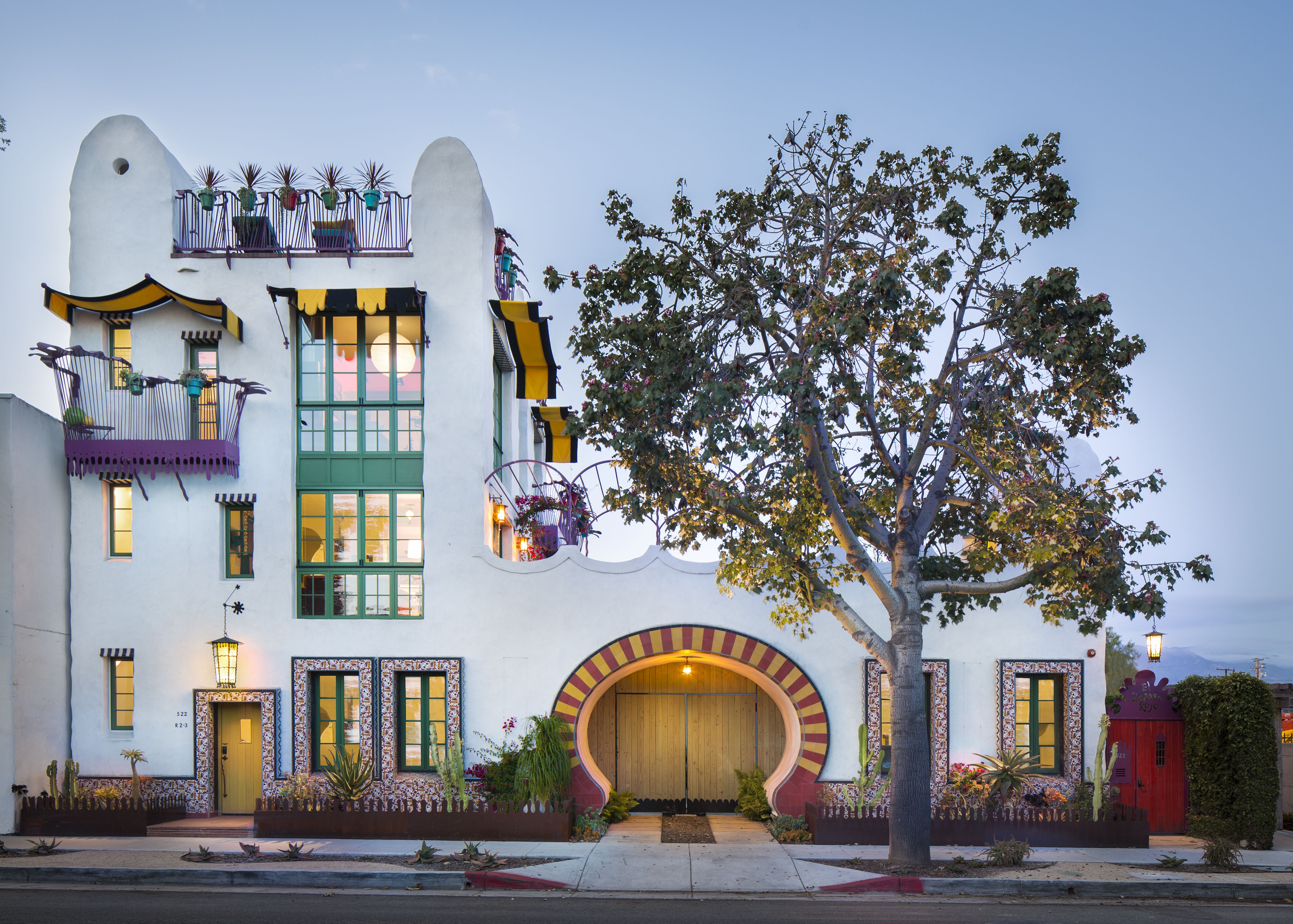 A fun and interesting looking building with a beautiful tree in front and lots of tile and balconies