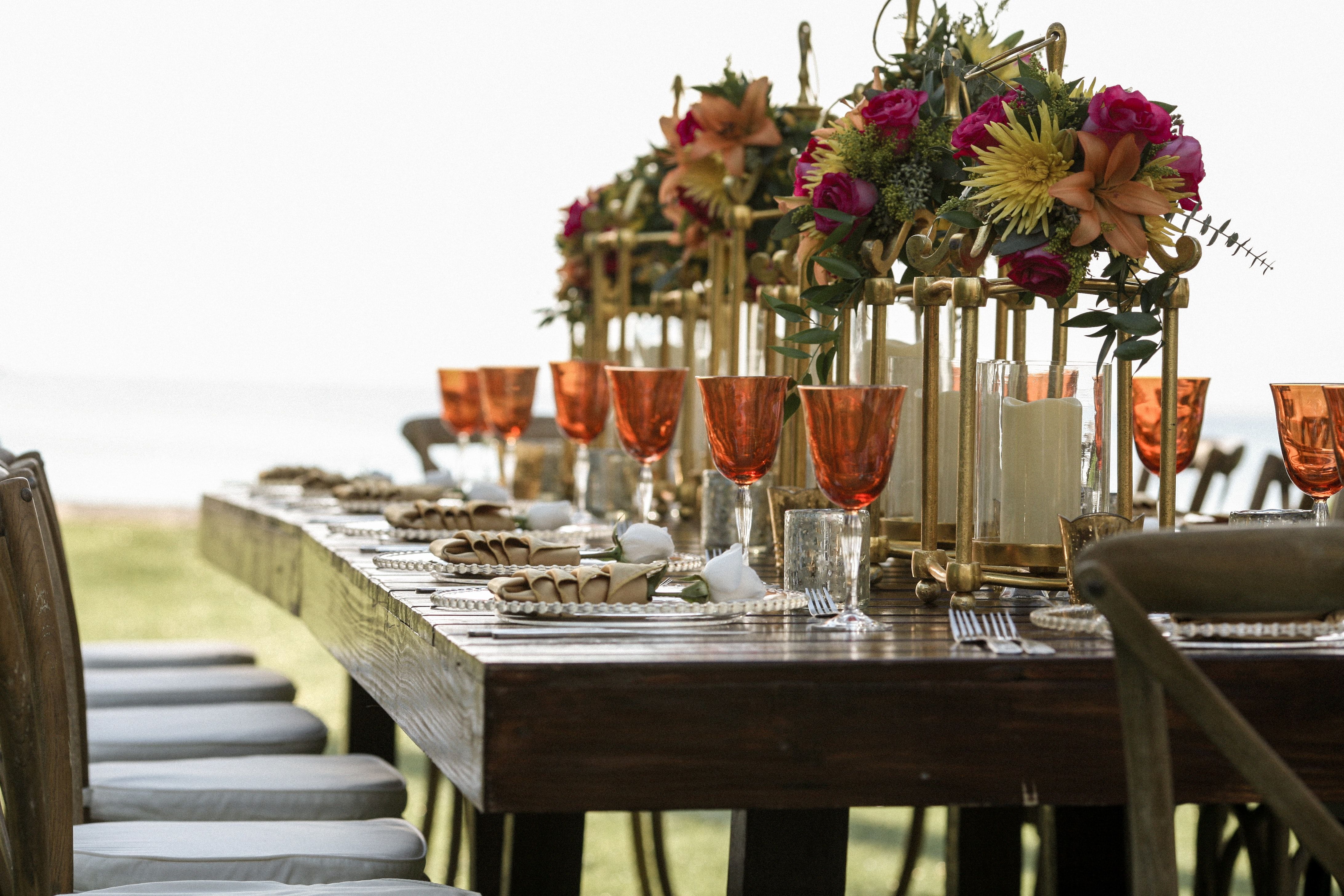 Rustic outdoor dining table on the grass set with wine glasses, place settings and flowers