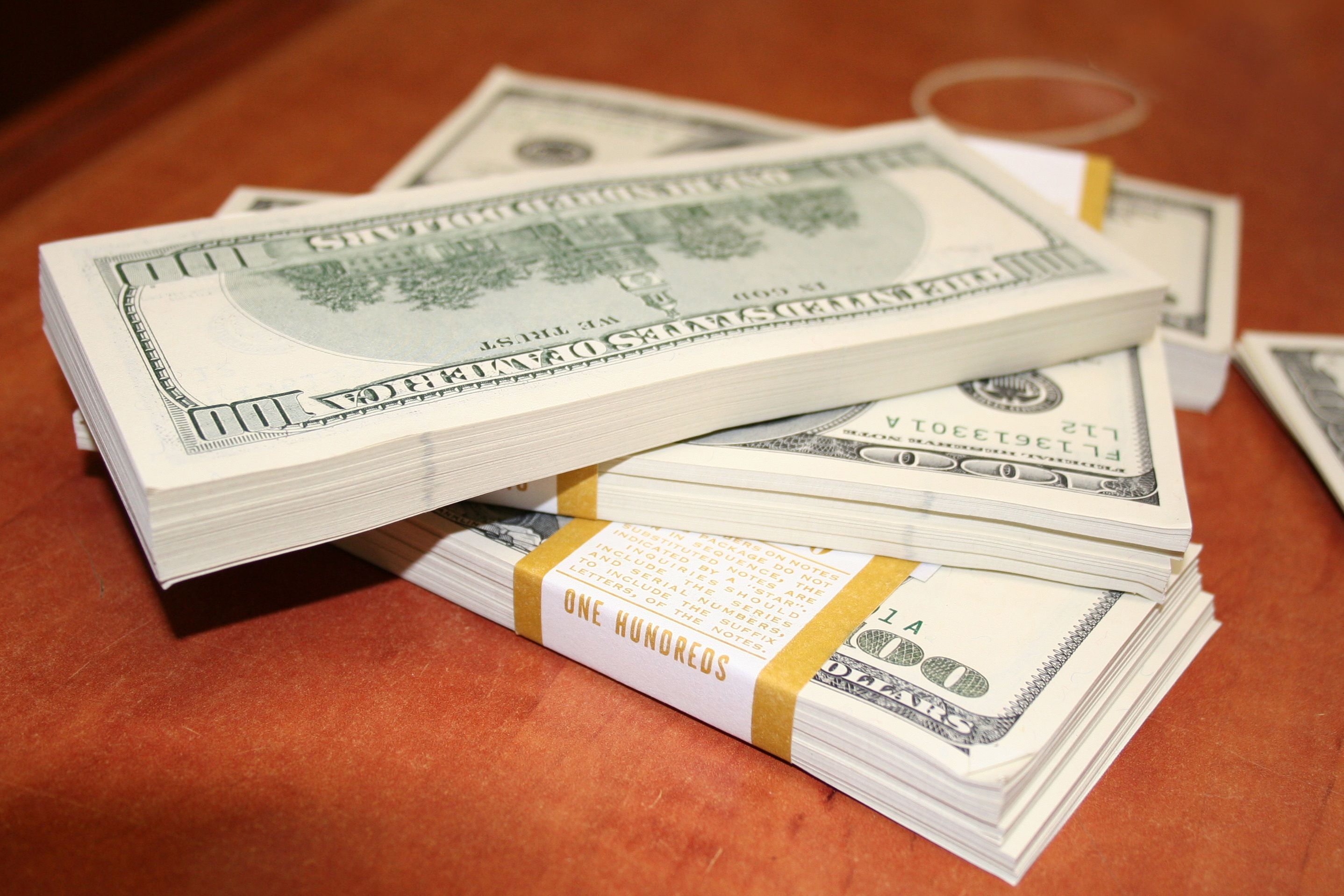 Three tightly-wrapped bundles of $100 bills on an orange table