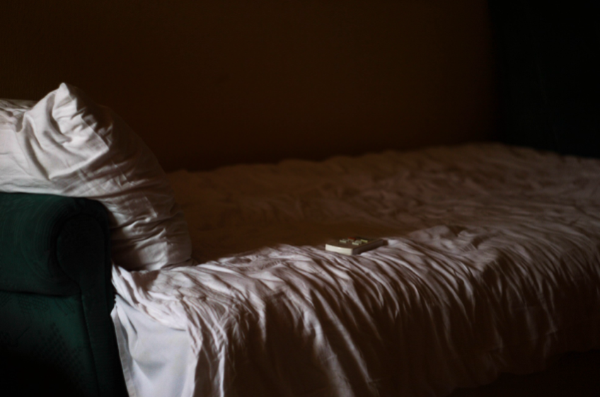 A bed with sheets askew in a dark room.