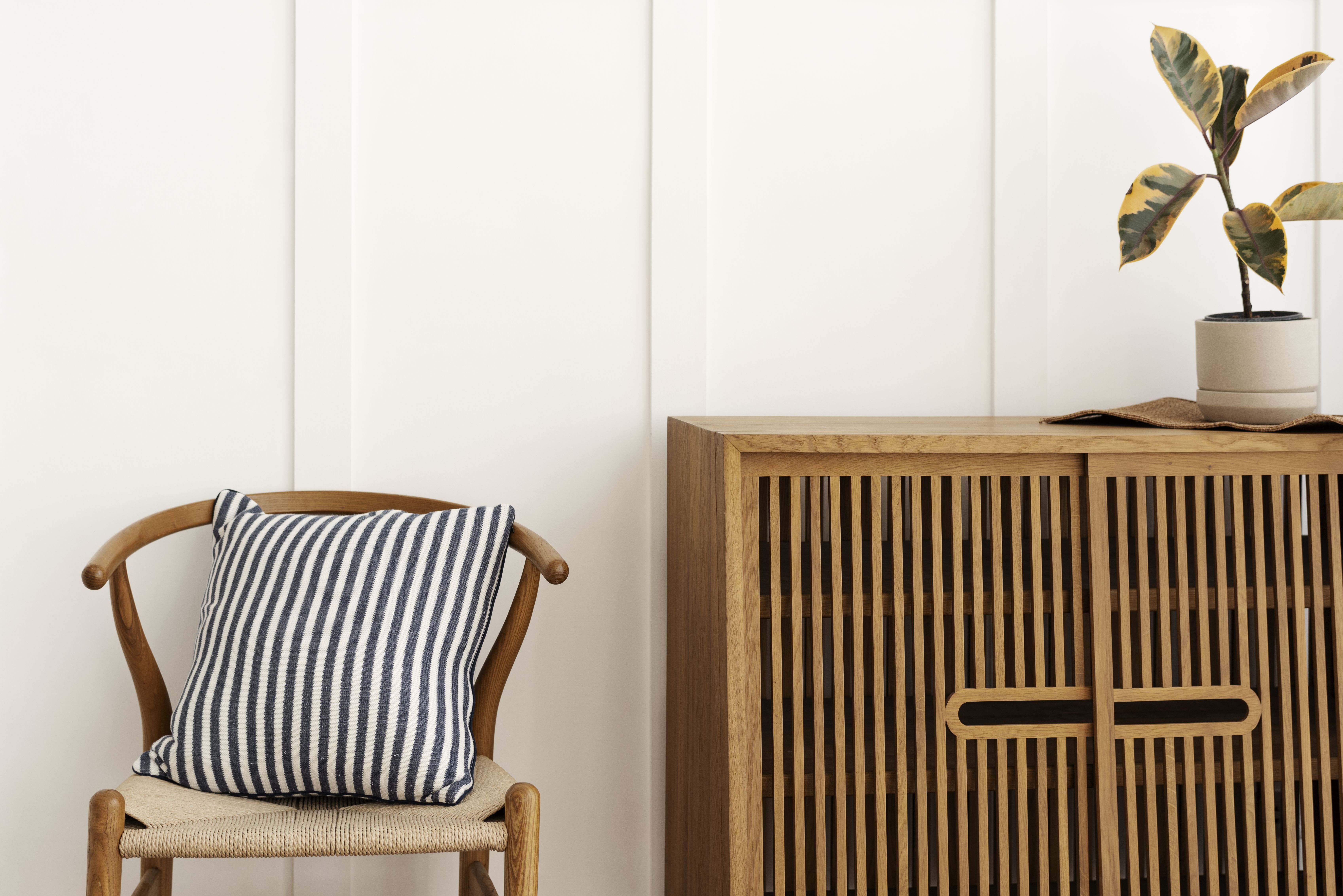 Mid-century chair with striped pillow next to a mid-century style cabinet with a houseplant on top.