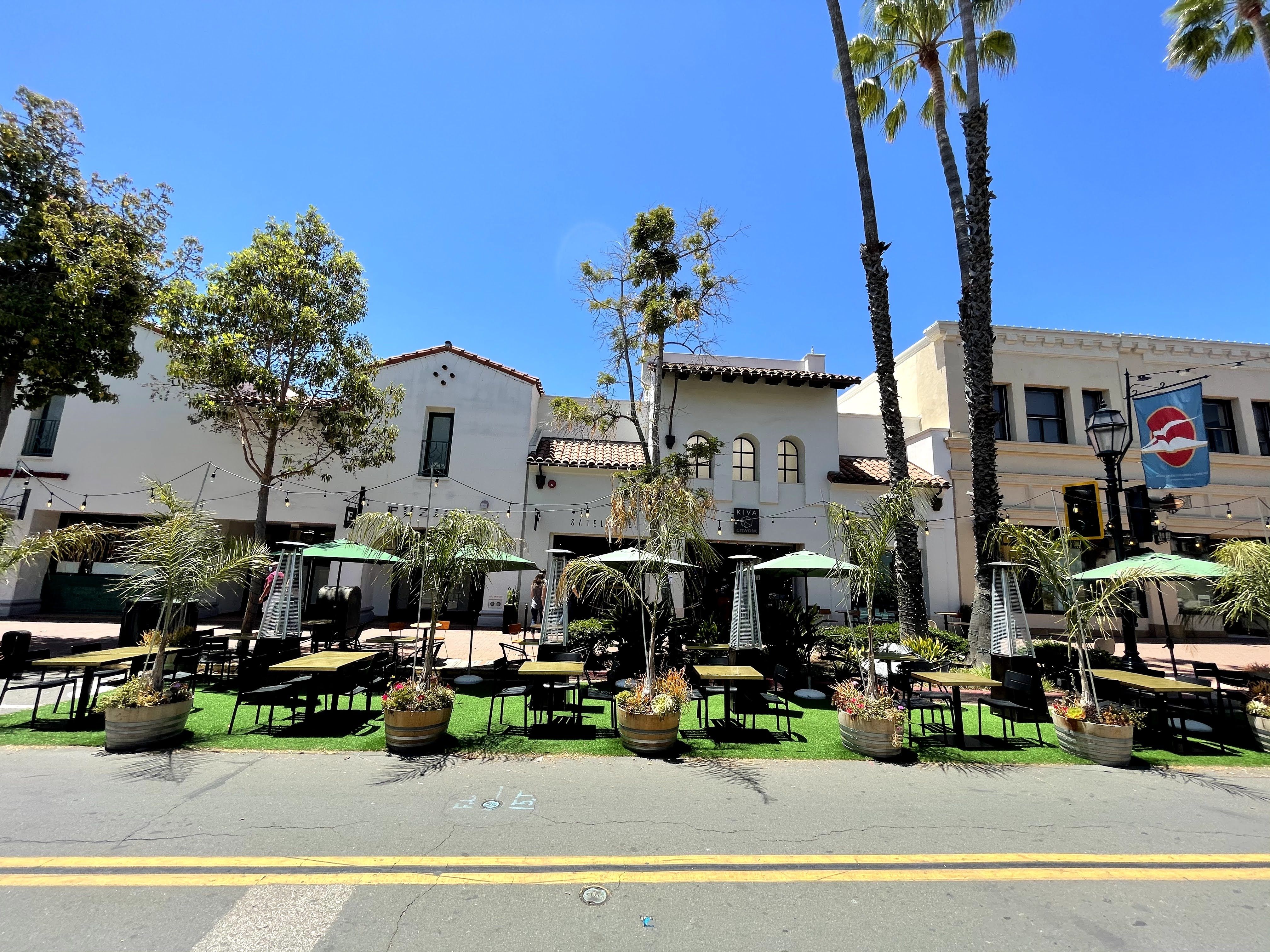 A huge outdoor patio where a street used to be with fake grass, tables, chairs and outdoor umbrellas and lights