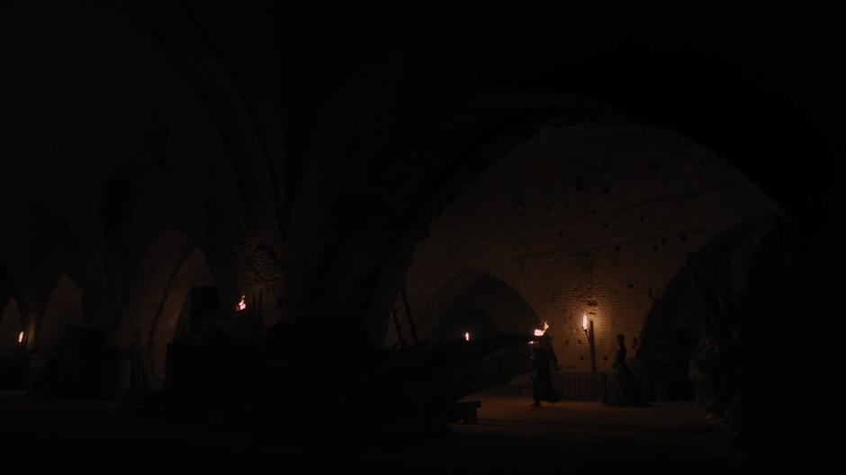 Qyburn leads Cersei through the dungeon with a torch.