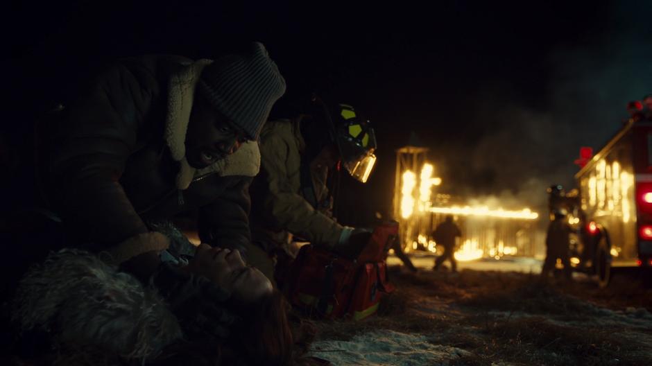 Dolls kneels over Wynonna and tries to wake her up while Ewan prepares his medical kit and the church burns in the background.