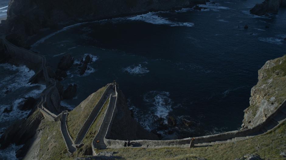 Davos and Jon walk down the steps while Missandei stands below looking out over the sea.