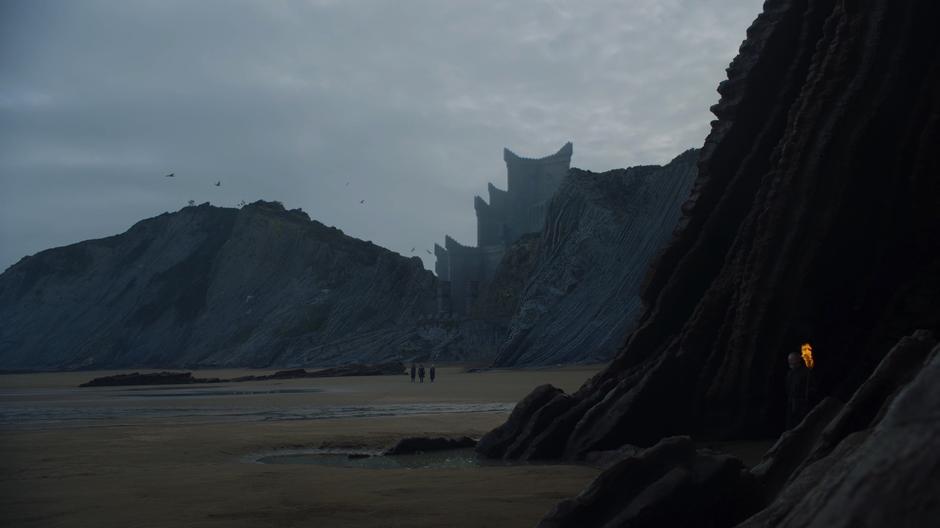 Jon leads Missandei and Dany across the beach to the distant cliff.