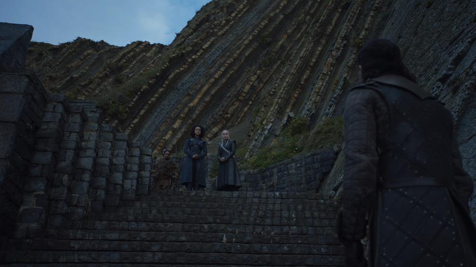 Jon looks up the steps to where Missandei and Daenerys are talking.