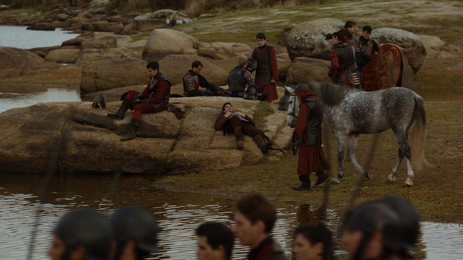 Several Lannister soldiers lounge by the edge of the water.