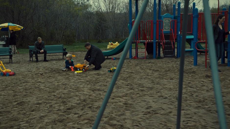 Jonathan watches a child play with their father on the playground.