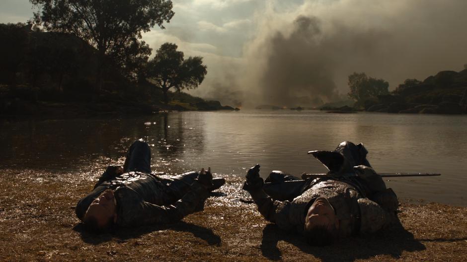 Bronn and Jaime lie on the back next to the river while the battleground continues to burn behind them.