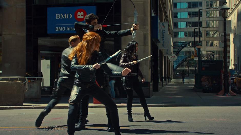 Clary, Jace, and Izzy stand ready while Alec takes aim at the demon with his bow.