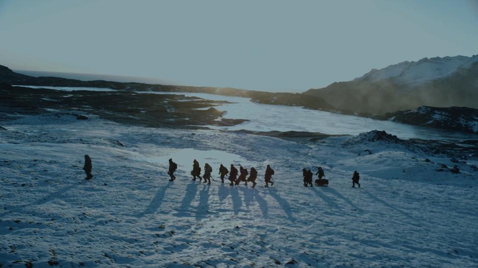 The party continues across the hillside in front of a frozen lake as the sun sits above the horizon behind them.