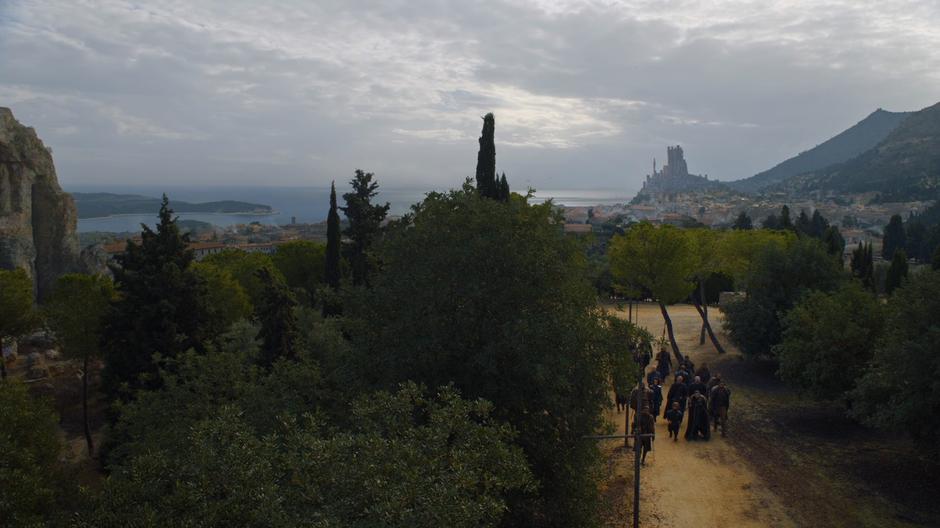 The party walks through the trees while the bulk if King's Landing sits in the distance.