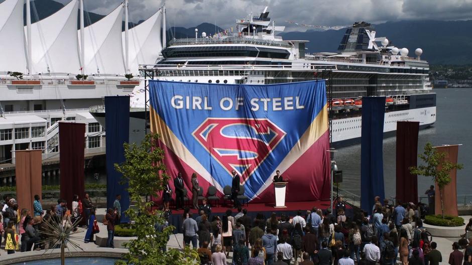 Lena starts her speech in front of the covered Supergirl statue.