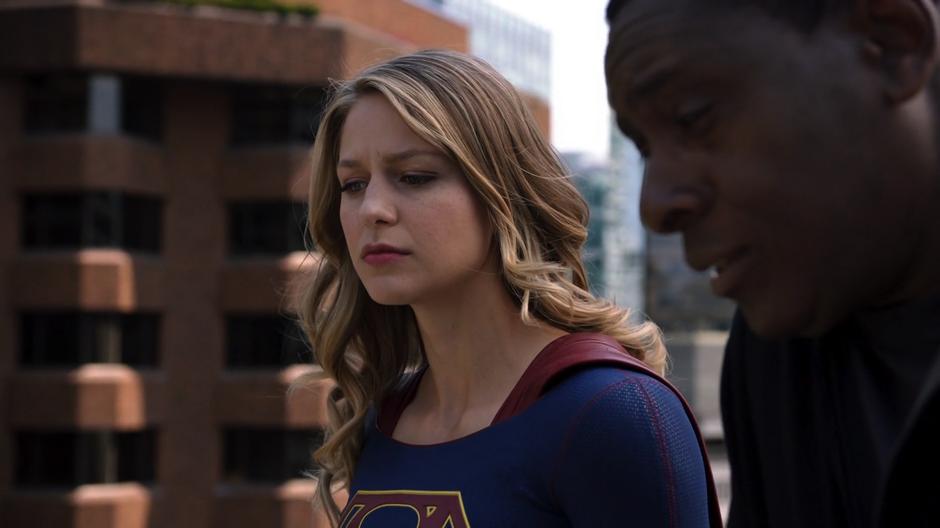 Kara and J'onn look back down at the plaza after chatting.