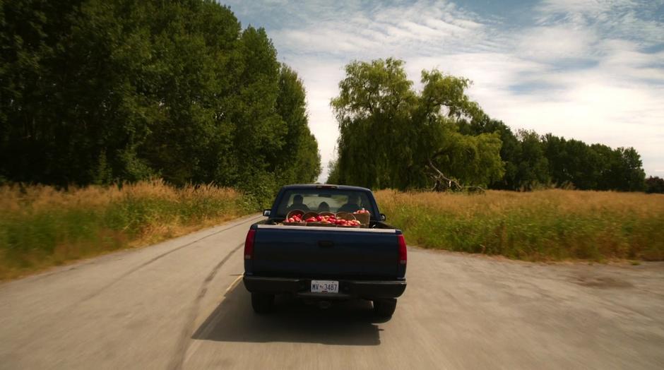 A pickup truck carrying apples drives down a two lane road.