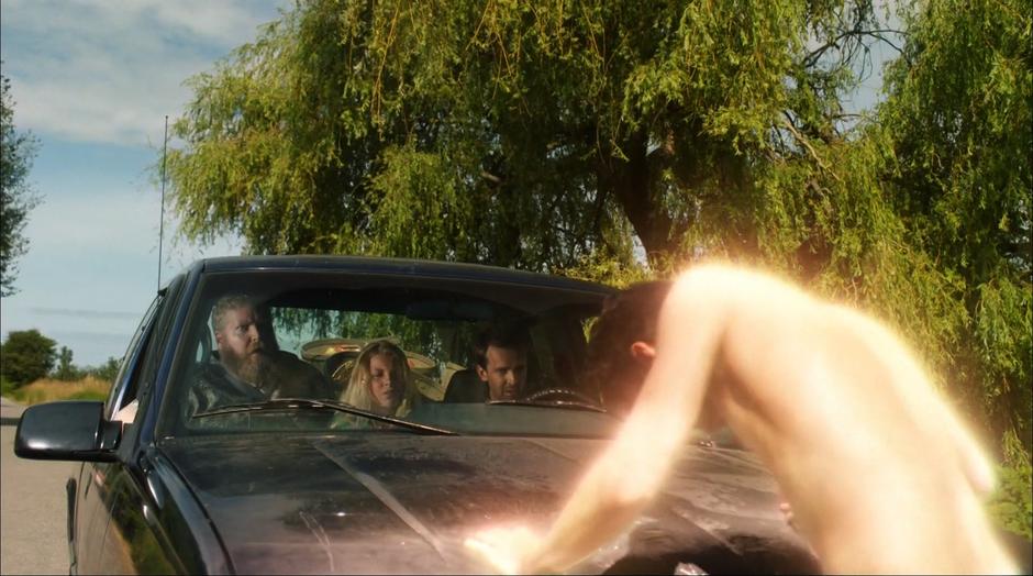 A very naked Barry leans on the front of the pickup truck while the family inside looks out at him.