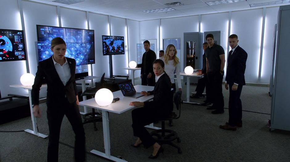 Ava Sharpe, Nate, Sara, Ray, Rip, and some agents react as Mick appears in the room with a Caesar.