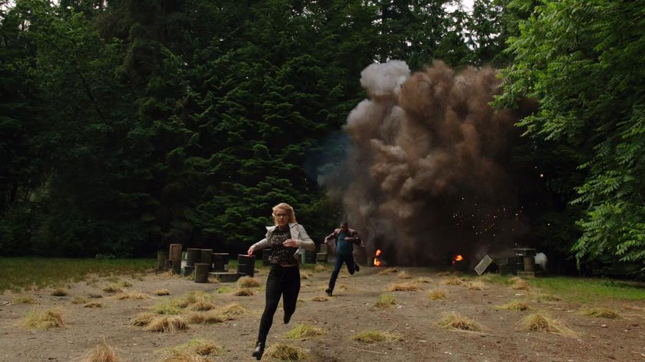 Felicity and Diggle run away from the explosions erupting behind them.