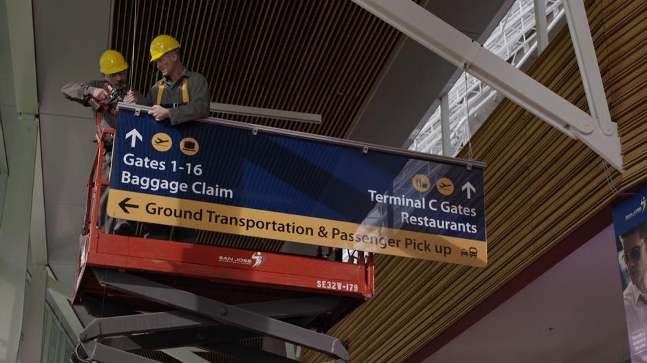 Two workers repair a sign high above the airport concourse.