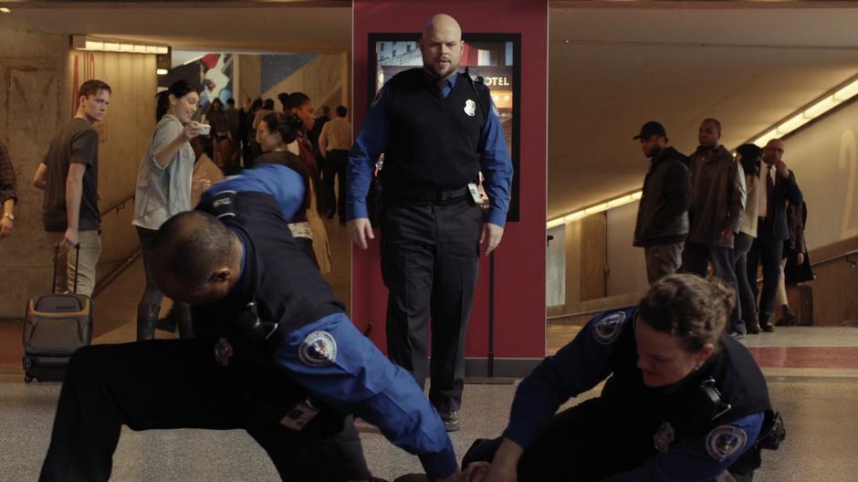 A third TSA agent approaches while two others hold Shaun to the ground.