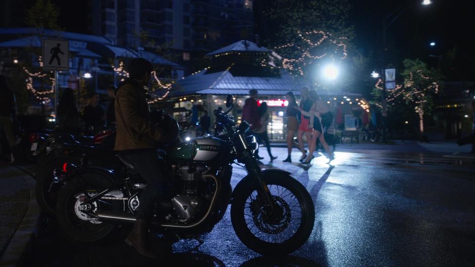 Oliver watches three pretty women walk across the street while sitting on his motorcycle.