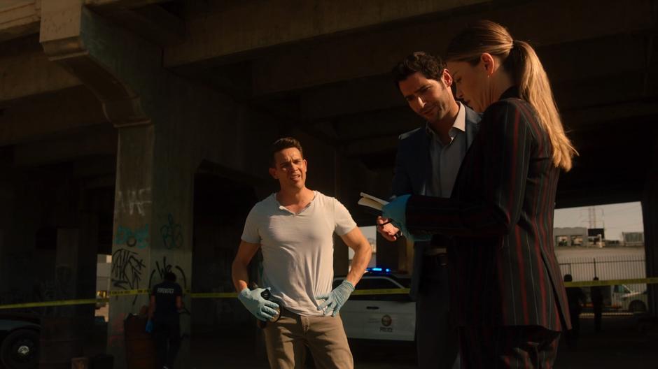 Lucifer and Chloe examine a notebook while Dan watches.