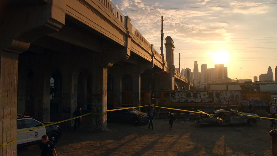 Lucifer holds up the police tape while ducking under with Chloe.