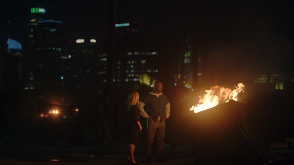 Linda and Amenadiel watch the old wings burn in a dumpster.