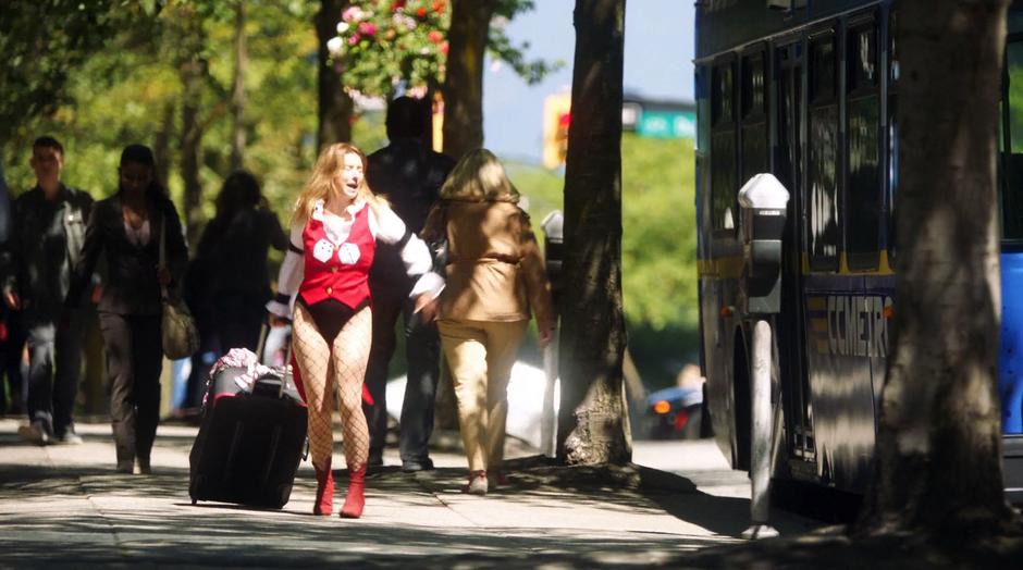 Rebecca Sharpe rushes down the street towards the bus while dragging her big suitcase.