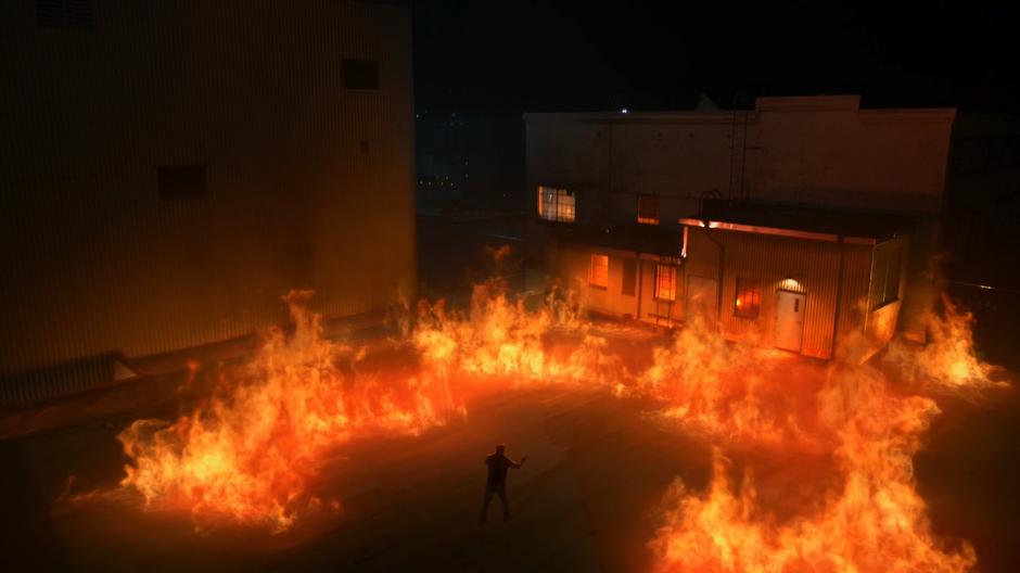 A man stands in the middle of a ring of fire on the burning roof of the factory.