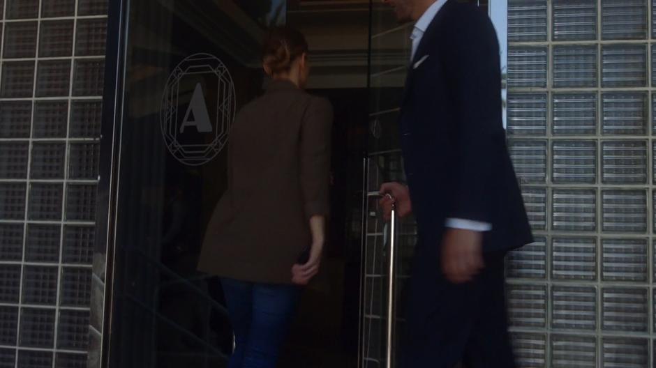 Lucifer holds the door open for Chloe as they enter the hotel lobby.