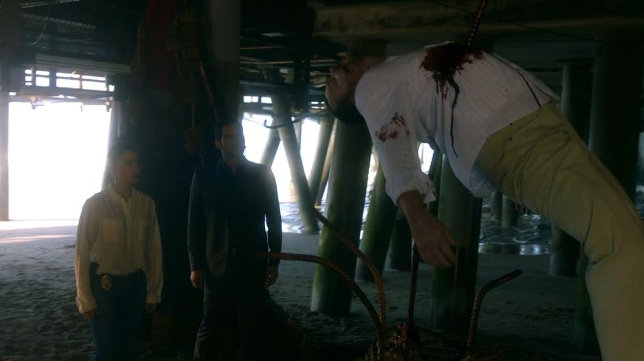 Chloe and Lucifer look at the body of their former suspect impaled under the pier.