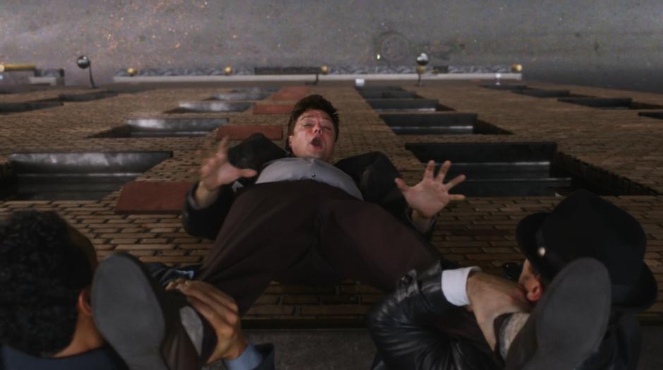Ralph Dibny is held over the side of the building by two goons.
