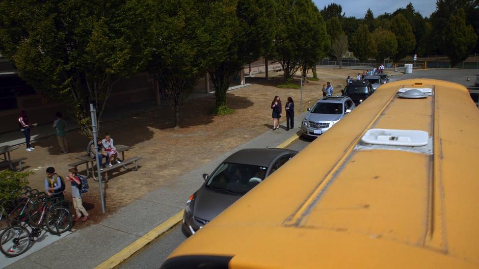 Cars and a bus pull up in front of the school to drop off kids.