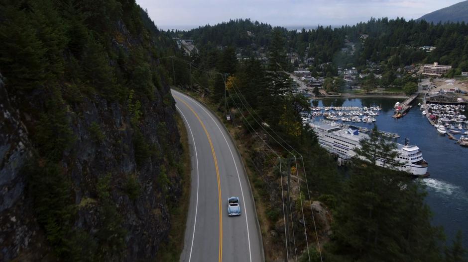 Kara and Alex drive down the highway as the Midvale harbor is visible below.