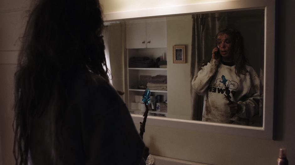 Suzie talks to Tina on the phone while standing in front of the bathroom mirror.