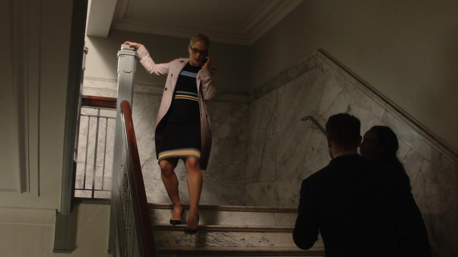Felicity walks down the stairs to the courtroom while talking to Curtis on the phone.