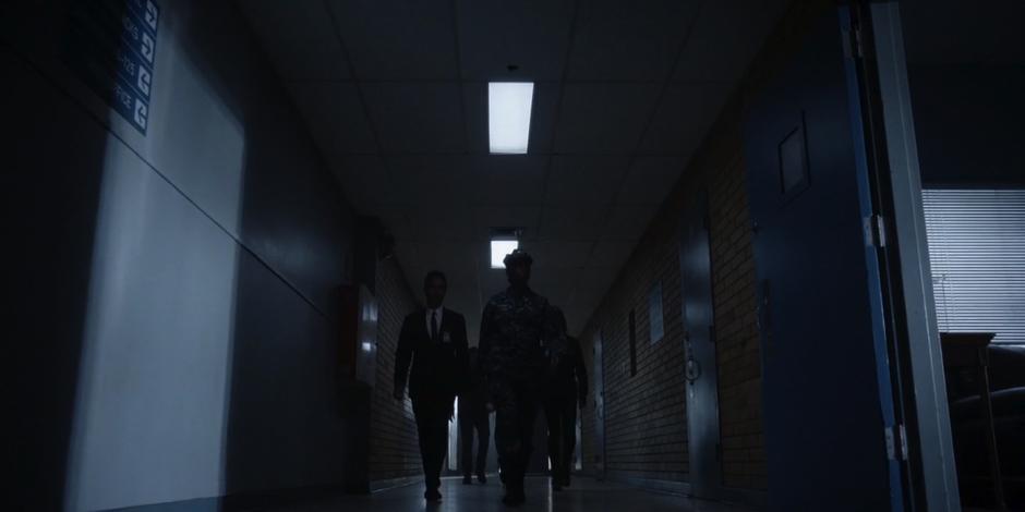 A navy ensign leads the team down the hallway to the base commander's office.