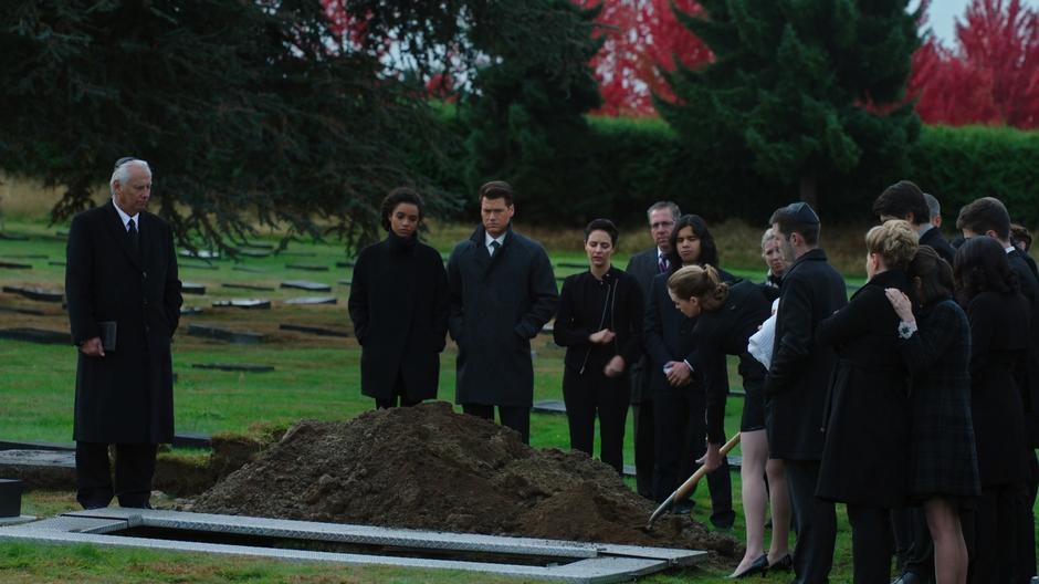 Caitlin shovels a bit of dirt to toss onto the coffin while the other mourners stand around.