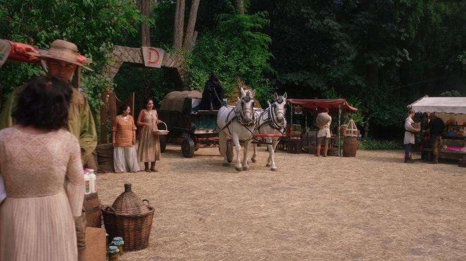A cart led by a figure hooded in black drives into the village square.