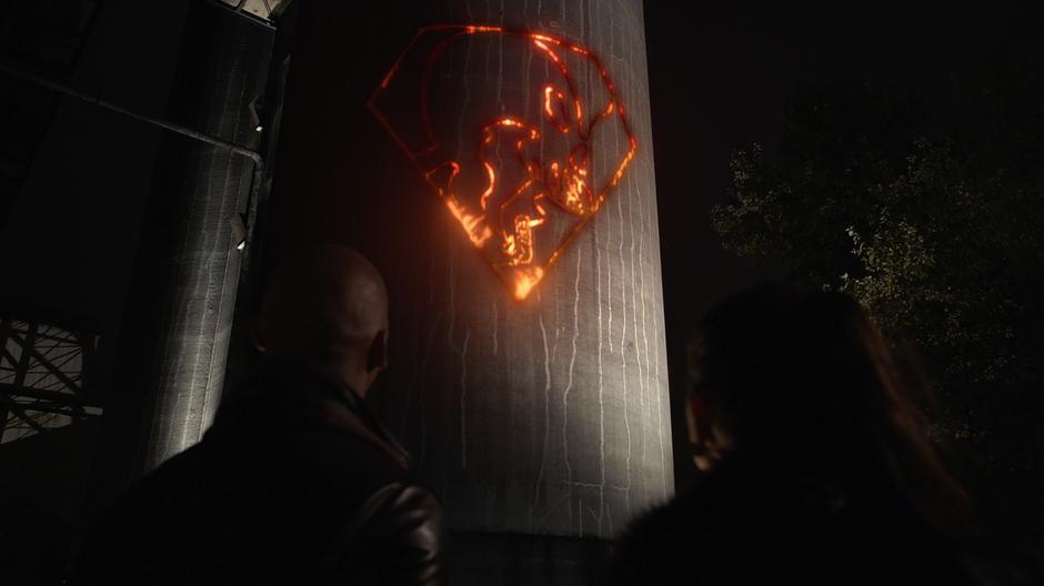 James and Lena look up at the mysterious symbol burned into the side of a building.