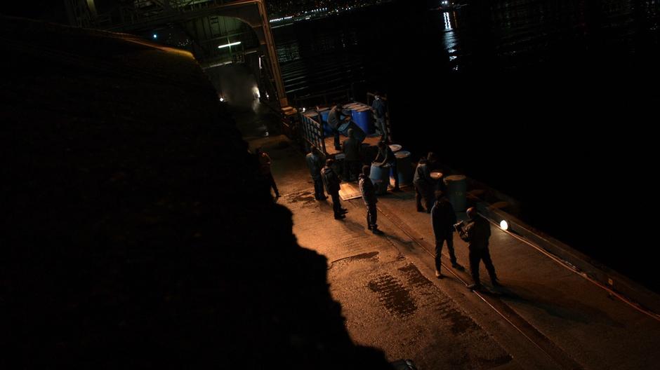 A guy holds up a bundle of money to the gang members who are unloading stuff from a truck.