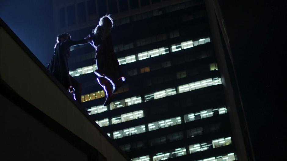 Reign holds Kara out over the edge of the building.